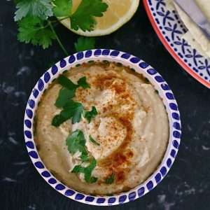 sesame tree hummus dip in blue patterned bowl with lemon and parsley