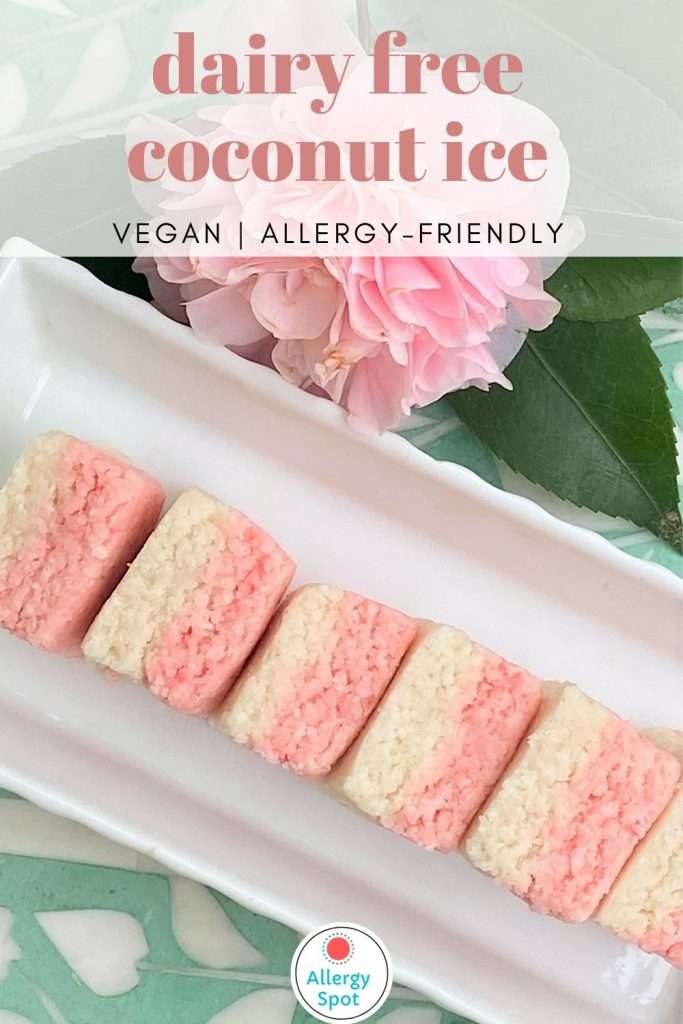 Pink and white dairy free coconut ice slice on a white dish with a pink camellia on a green bone inlay table with text overlay "dairy free coconut ice vegan allergy-friendly"