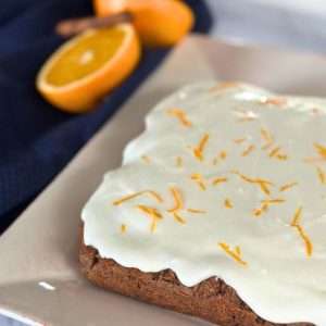nut and gluten free carrot cake with orange and ginger on white plate with fresh oranges and cinnamon stick