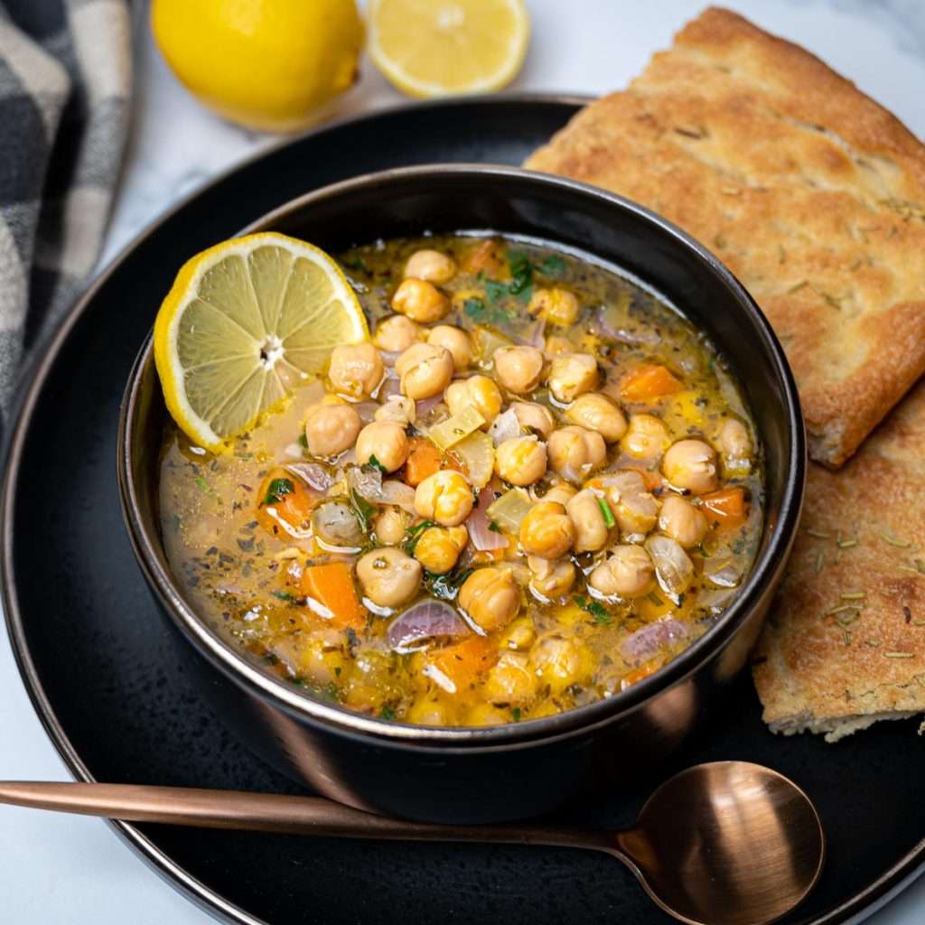 allergy friendly Greek chickpea soup with lemon in black bowl with lemon slices and bread