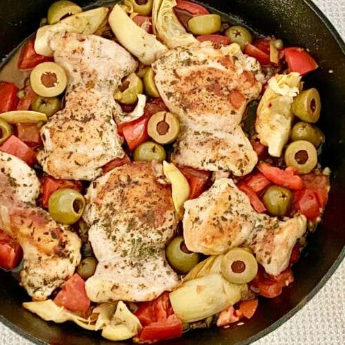 Greek chicken thighs with olives, tomato and artichokes in a cast iron pan