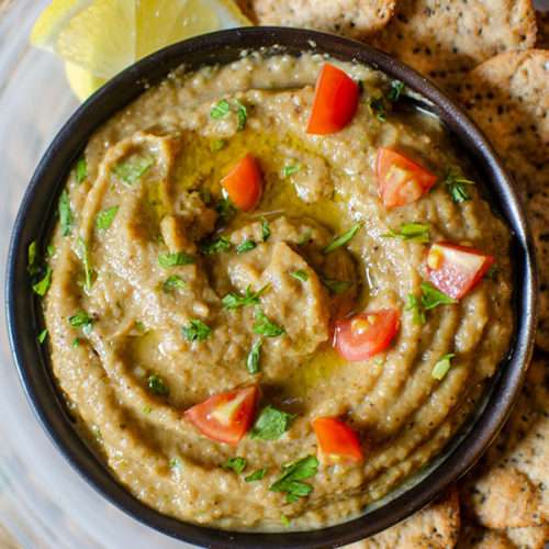 Melitzanosalata Greek eggplant dip in black bowl with lemon and crackers